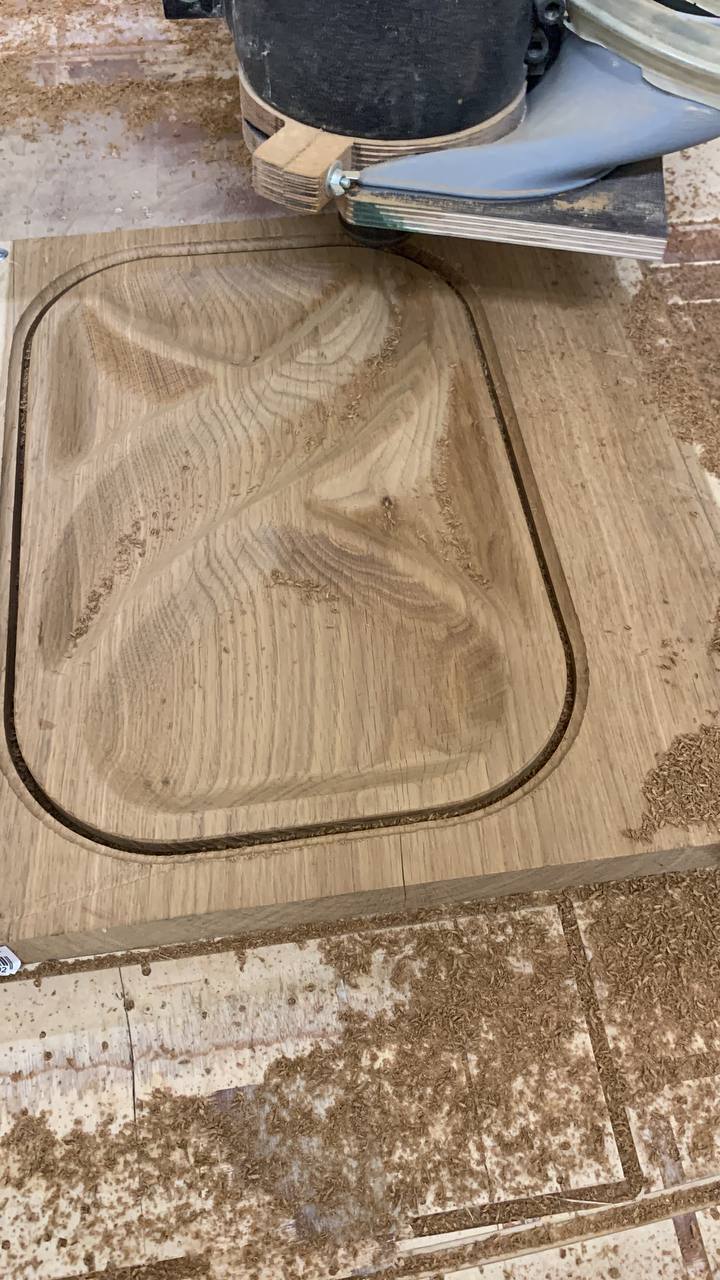 CNC-kone jyrsimässä tammea pähkinätarjottimen muotoon, lastuja näkyvissä.